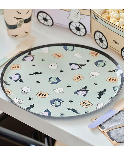 A stack of colorful ghost-patterned Boo Crew paper plates arranged neatly on a dark wooden Halloween buffet table next to seasonal treats.