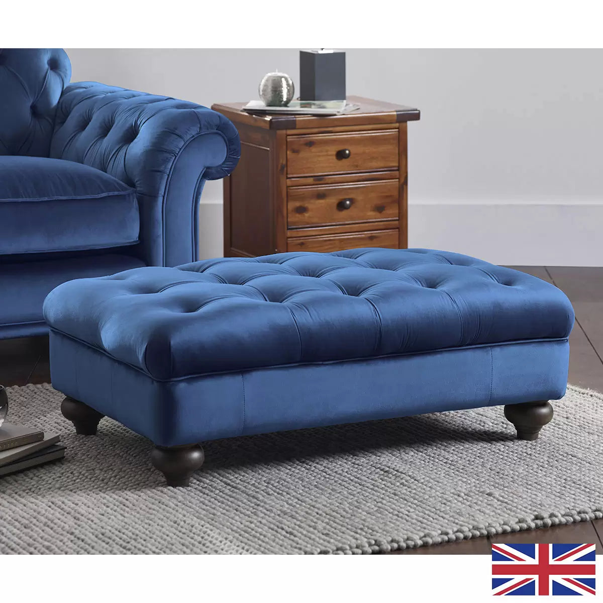 Front angle view of the Bordeaux Blue Velvet Footstool featuring deep hand-tied tufting and dark wood legs on a light timber floor.