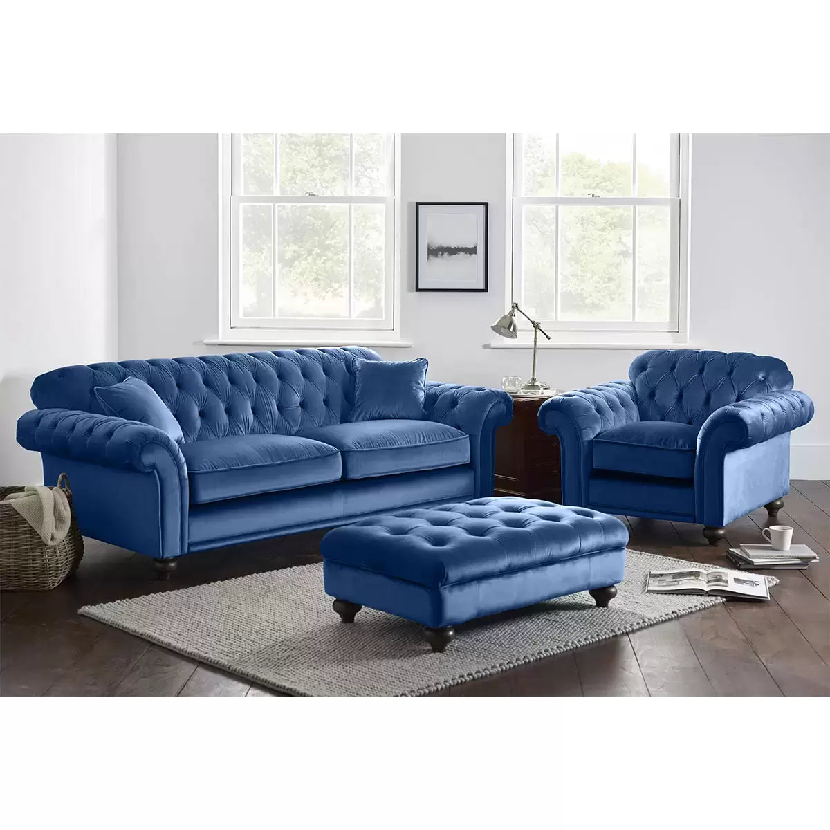 Front angle view of the Bordeaux Blue Velvet Footstool featuring deep hand-tied tufting and dark wood legs on a light timber floor.