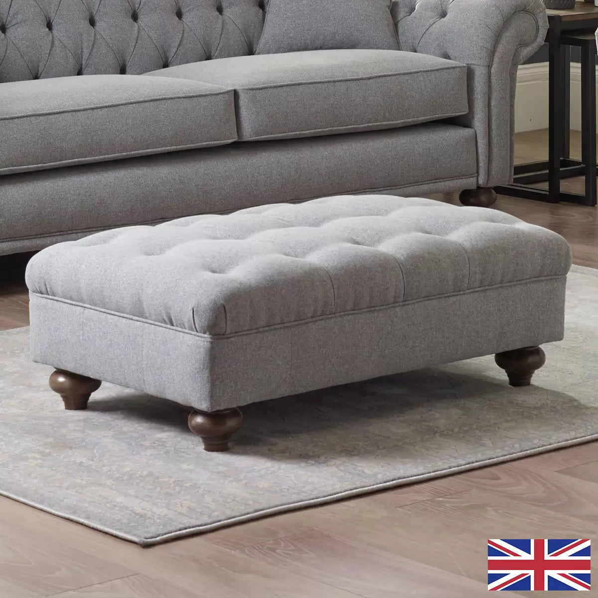 Close-up angle of the grey Bordeaux fabric footstool showing hand-tied button detailing, linen texture, and dark stained wooden legs in a living room setting.
