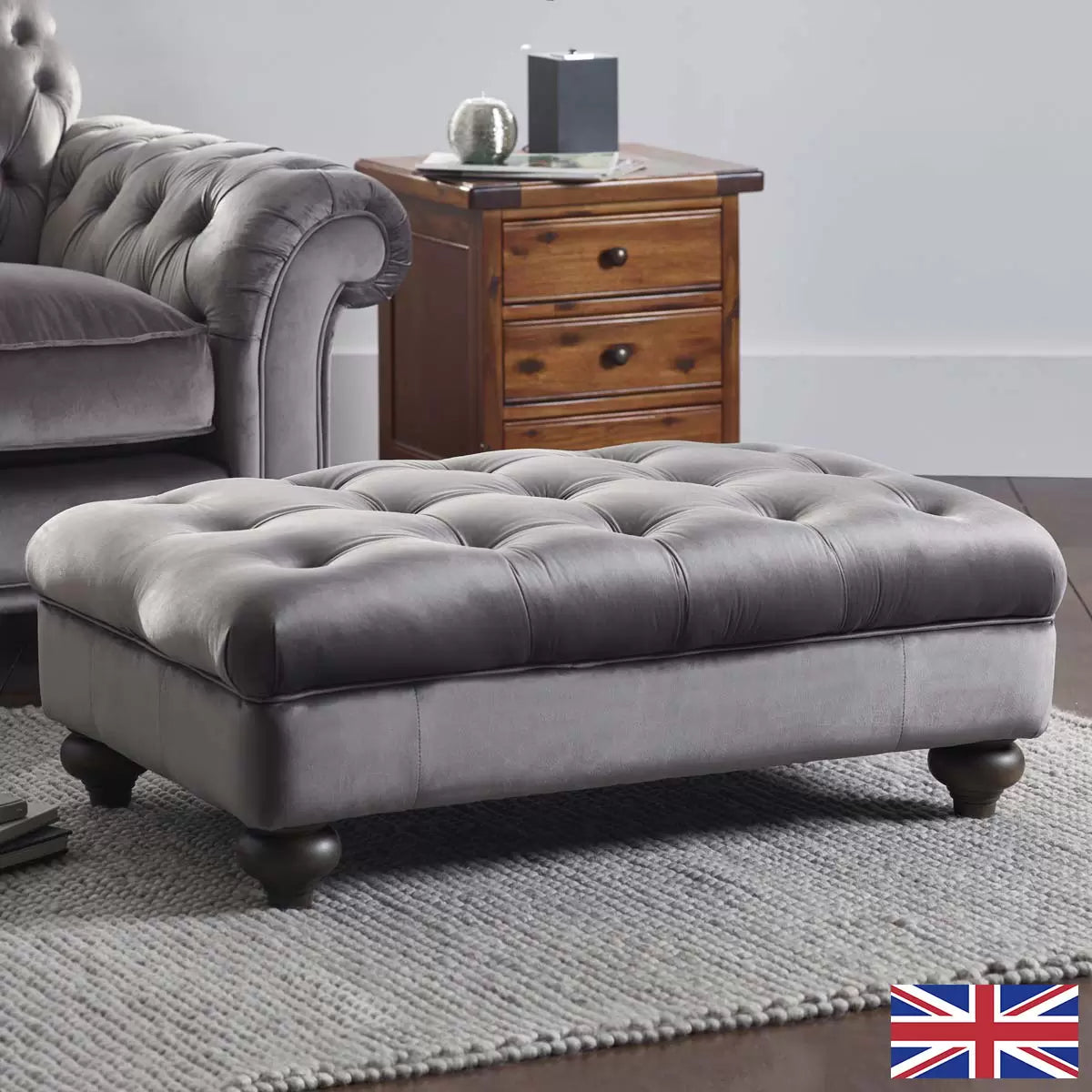 Front angle view of the Bordeaux Grey Velvet Footstool featuring deep hand-tied tufting and dark stained solid wood legs in a modern living room setting.