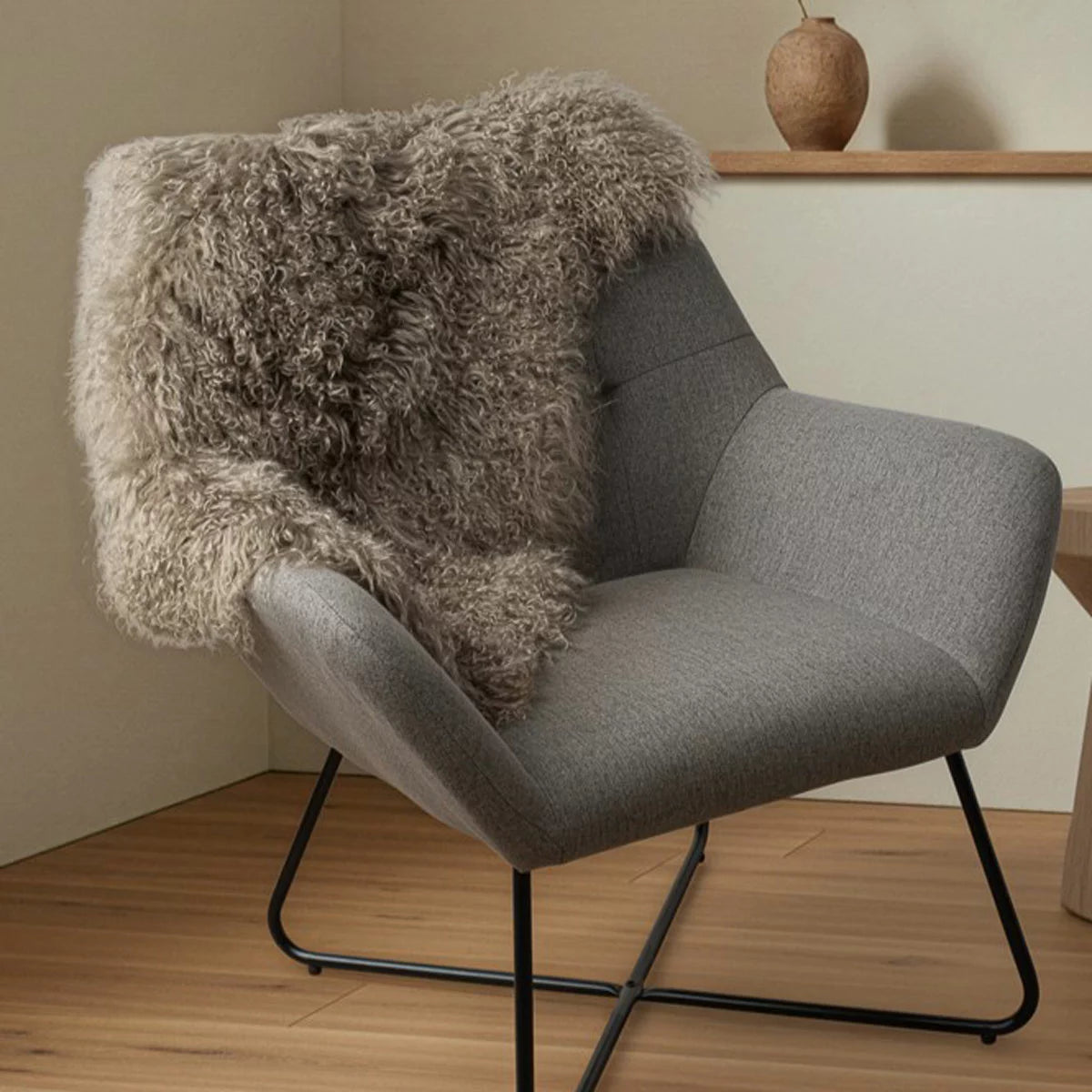 Overhead shot of a soft white Bowron Tibetan Sheepskin Rug draped across a Scandinavian wooden armchair showing long, silky wool curls.