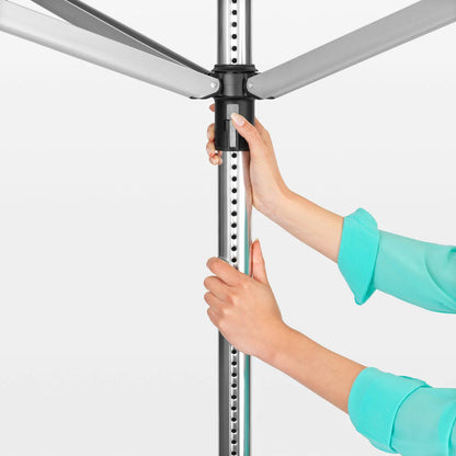 A Brabantia Lift-O-Matic 50m rotary airer standing in a well-maintained garden, featuring taut lines and a protective cover nearby on a clear, sunny day.