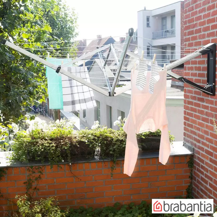 A folded Brabantia Wallfix 24m clothes airer mounted on a brick wall with its black protective cover.