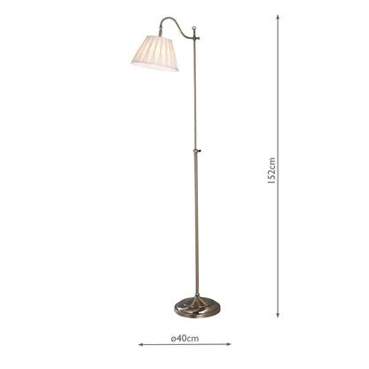 Side view of the Suffolk Rise and Fall Floor Lamp in antique brass, showcasing its adjustable height mechanism and cream pleated faux silk shade next to a classic armchair.