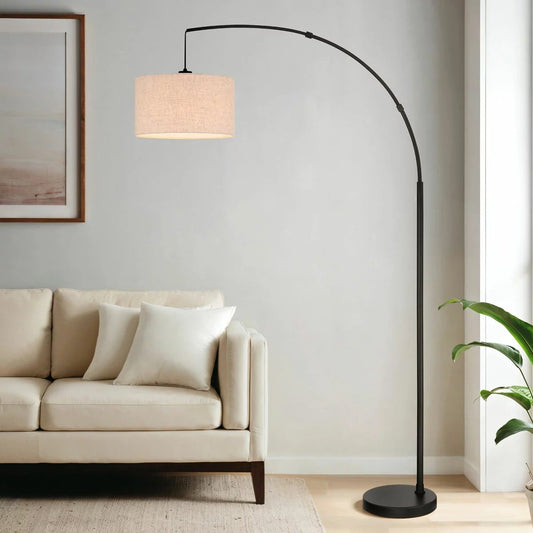 Bridgeport Designs Madrid Arc Floor Lamp with matte black steel finish and tan linen drum shade standing in a modern living room setting.