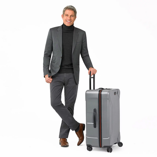 Textured dark metallic Briggs & Riley Torq 78cm Large Spinner Suitcase with molded handles and four dual ball-bearing spinner wheels standing upright on an airport terminal floor.