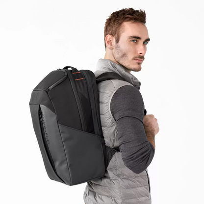 Black Briggs & Riley ZDX Cargo Backpack showcasing top cargo pocket, side zip compartments, and water-resistant PVC base resting on a wooden surface.