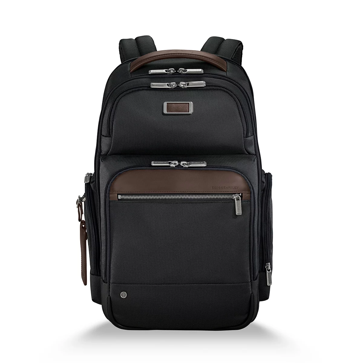 Front three-quarter view of the black ballistic nylon Briggs and Riley at work Cargo Backpack standing upright on a minimalist wooden office desk next to a laptop.