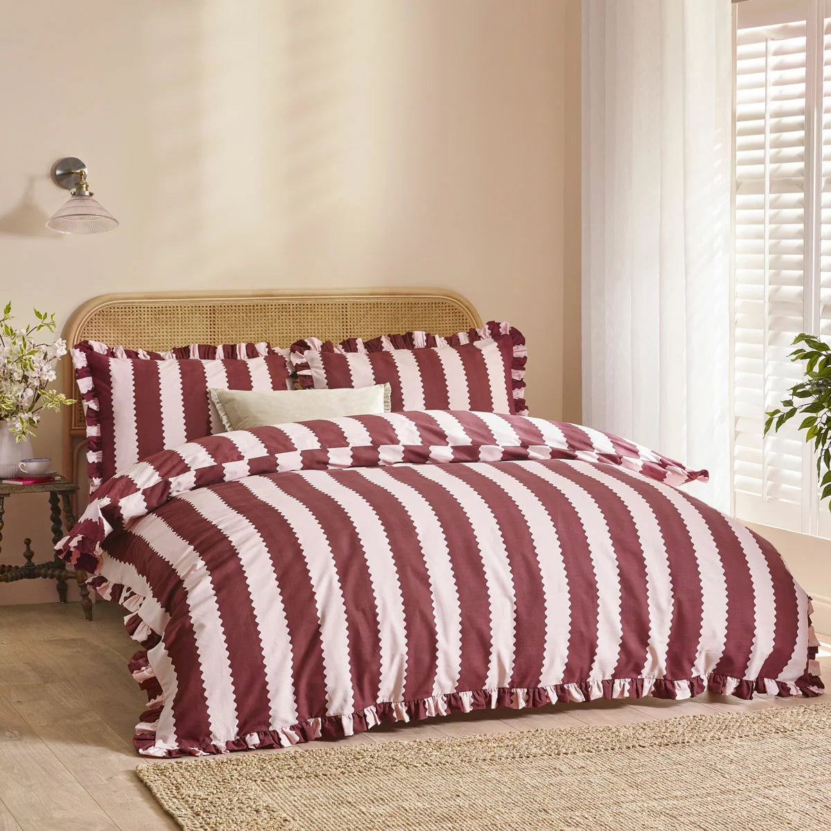 A cozy king bed dressed in the burgundy and white striped Wylder Birdie duvet cover, showing the delicate ruffled edges of the pillowcases resting in a country-style bedroom.