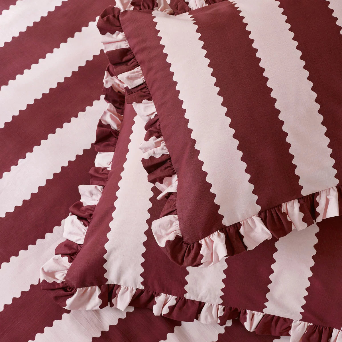 A cozy king bed dressed in the burgundy and white striped Wylder Birdie duvet cover, showing the delicate ruffled edges of the pillowcases resting in a country-style bedroom.