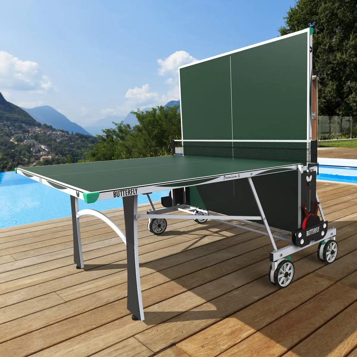 Full side view of the blue Butterfly Premium 4 Outdoor Table Tennis Table fully assembled on a backyard stone patio, showing its silver legs and matching green corner bumpers.