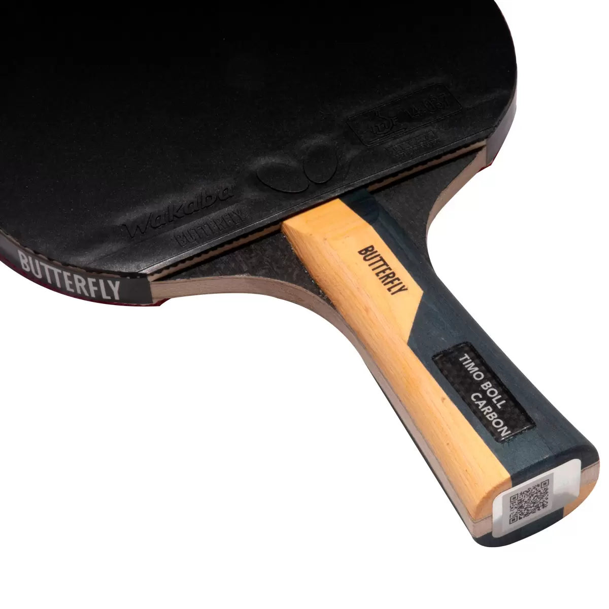 Profile view of the black and red Butterfly Timo Boll Carbon table tennis bat with a flared handle, resting on a blue indoor ping pong table next to six white 40+ training balls.