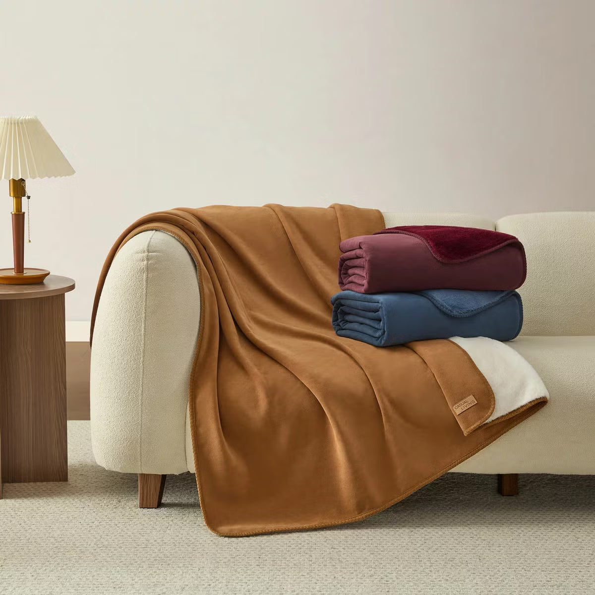 Soft Casual Living Luxe throw blanket folded on a modern sofa showing the velvety faux suede side, plush faux fur reverse, and whipstitched border detail.