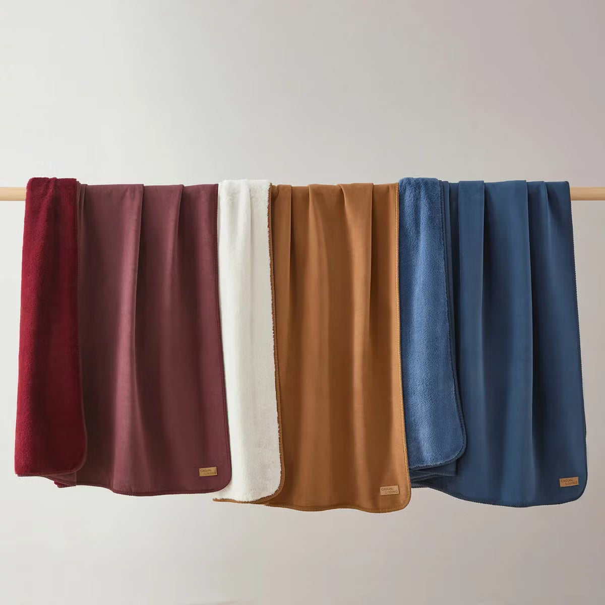 Soft Casual Living Luxe throw blanket folded on a modern sofa showing the velvety faux suede side, plush faux fur reverse, and whipstitched border detail.
