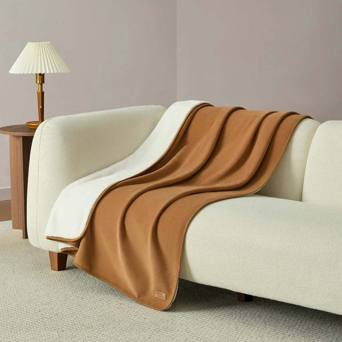 Soft Casual Living Luxe throw blanket folded on a modern sofa showing the velvety faux suede side, plush faux fur reverse, and whipstitched border detail.