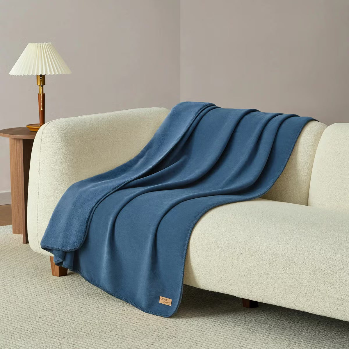 Soft Casual Living Luxe throw blanket folded on a modern sofa showing the velvety faux suede side, plush faux fur reverse, and whipstitched border detail.
