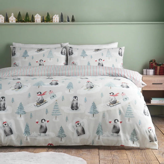 Catherine Lansfield festive Christmas penguins reversible brushed cotton duvet cover set with matching pillowcases folded neatly on a bed setting.