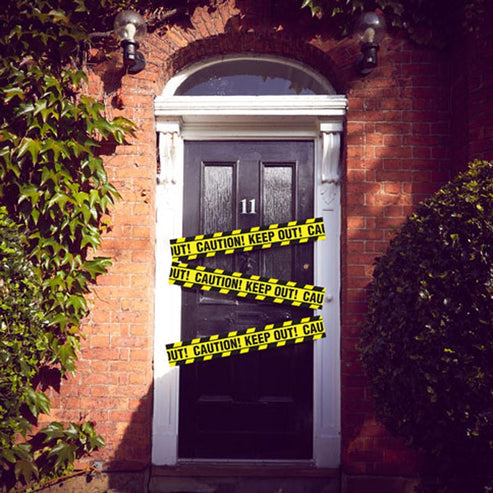 Bright yellow plastic caution tape stretched taut across a dark wooden doorway for party decoration.