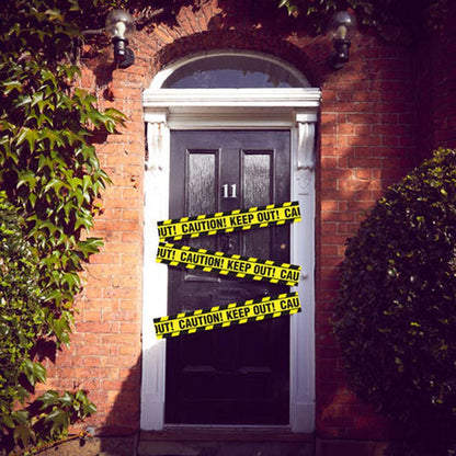 Bright yellow plastic caution tape stretched taut across a dark wooden doorway for party decoration.