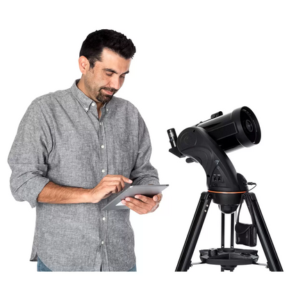 Three-quarter studio angle of the black Celestron Astro Fi 5 inch Schmidt-Cassegrain telescope mounted on its aluminum tripod with a smartphone docked onto the eyepiece adapter.