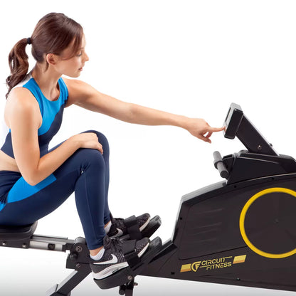 Black Circuit Fitness 986RW Deluxe Magnetic Folding Rowing Machine shown from a side angle with digital LCD console, foam handlebar, and extended steel rail set up in a modern home workout area.