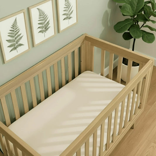 A pair of Clair De Lune organic cotton fitted cot bed sheets showing the elasticated edges and cream fabric knit.