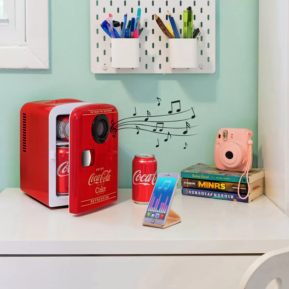 Front view of the vibrant red vintage Coca-Cola 4L mini fridge with retro latch handle, sitting on a modern wooden desk next to a smartphone.
