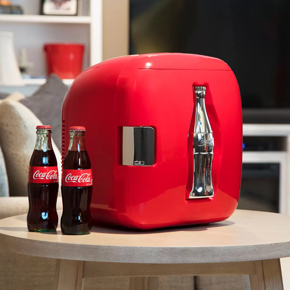 Front view of the compact red Coca-Cola Heritage 7.9L mini fridge on a sleek office shelf, highlighting the embossed 3D chrome contour bottle design on the door.