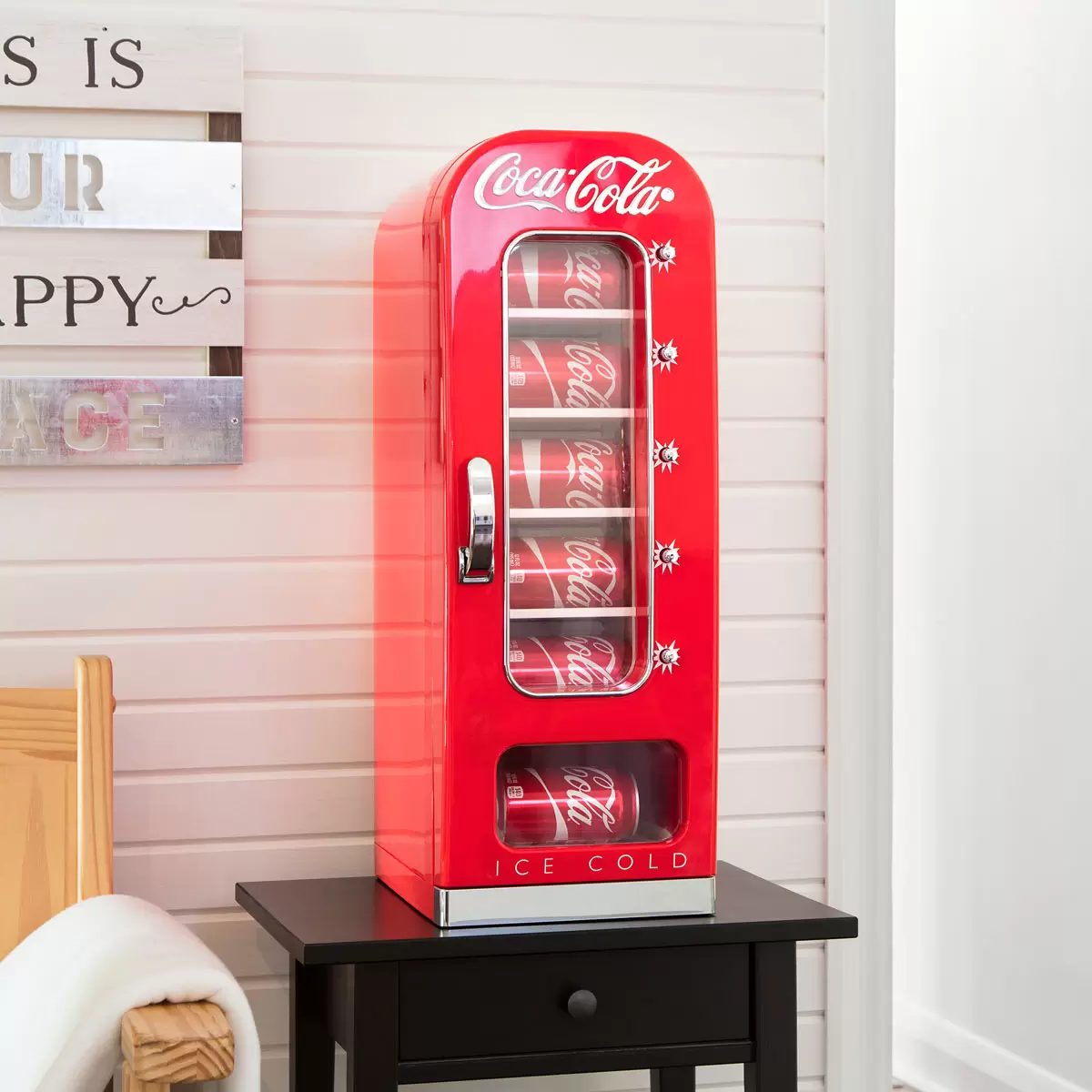 Front view of the vibrant red Coca Cola 5L mini fridge vending machine featuring a clear vertical display window full of cans, polished chrome accents, and retro artwork on a wooden desk.