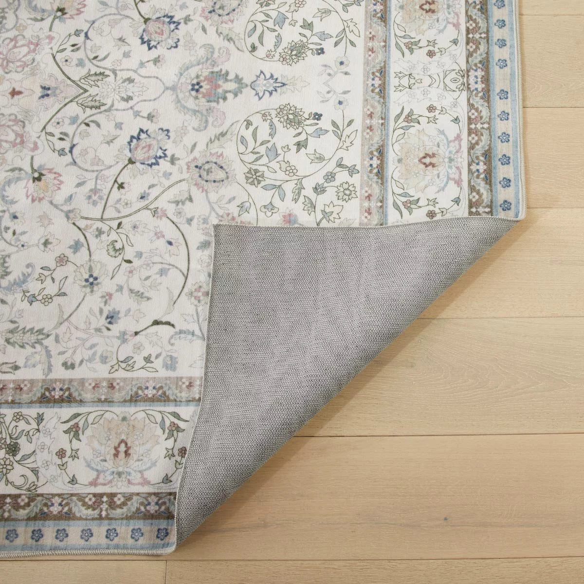 Top-down view of the soft pastel pink and grey Concept Looms Liberty Washable Rug resting smoothly on a light hardwood floor next to a modern sofa.