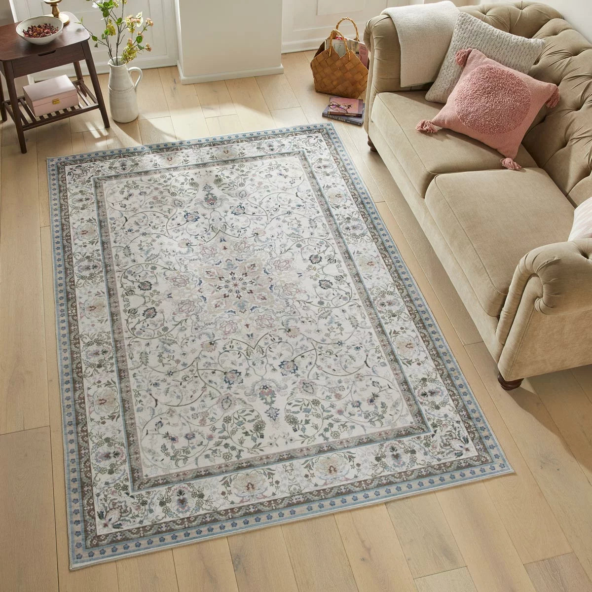 Top-down view of the soft pastel pink and grey Concept Looms Liberty Washable Rug resting smoothly on a light hardwood floor next to a modern sofa.