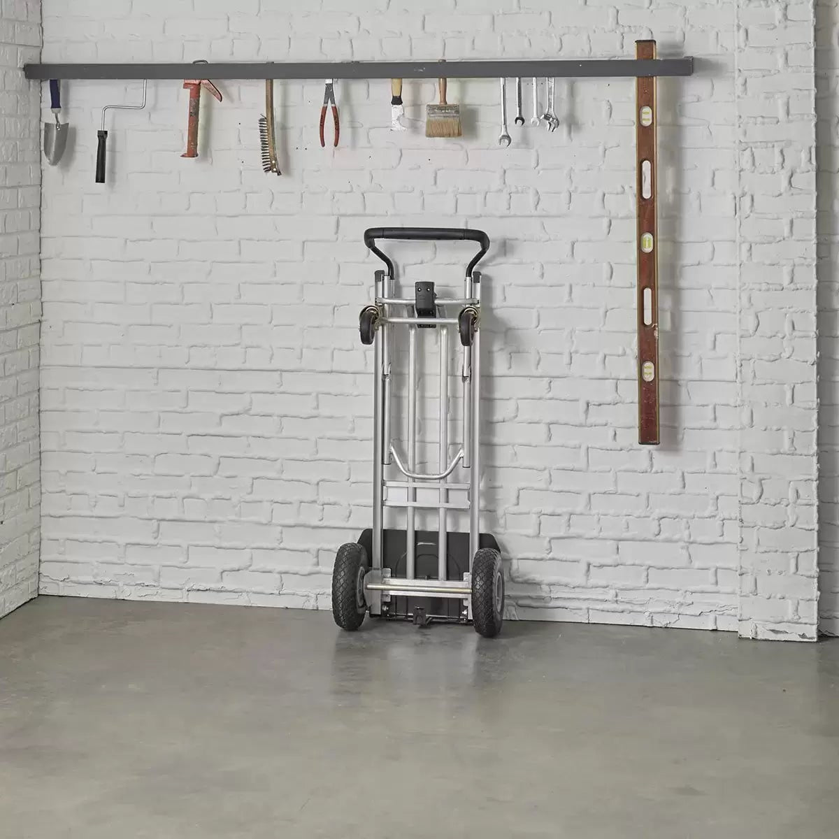 Black and silver Cosco 3-in-1 aluminium hand truck configured in the 4-wheel flatbed position showing the durable flat-free wheels on a smooth industrial concrete surface.