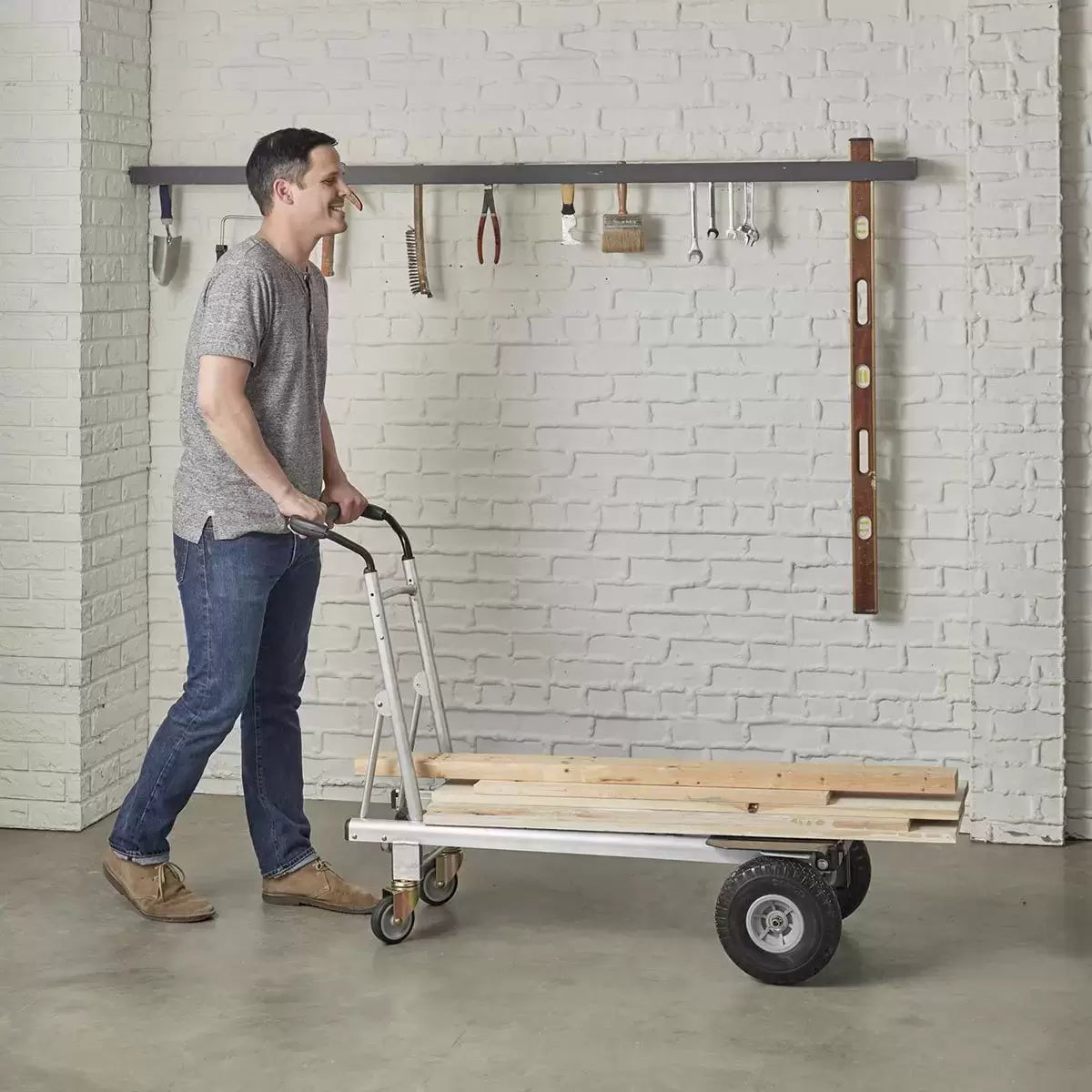 Black and silver Cosco 3-in-1 aluminium hand truck configured in the 4-wheel flatbed position showing the durable flat-free wheels on a smooth industrial concrete surface.