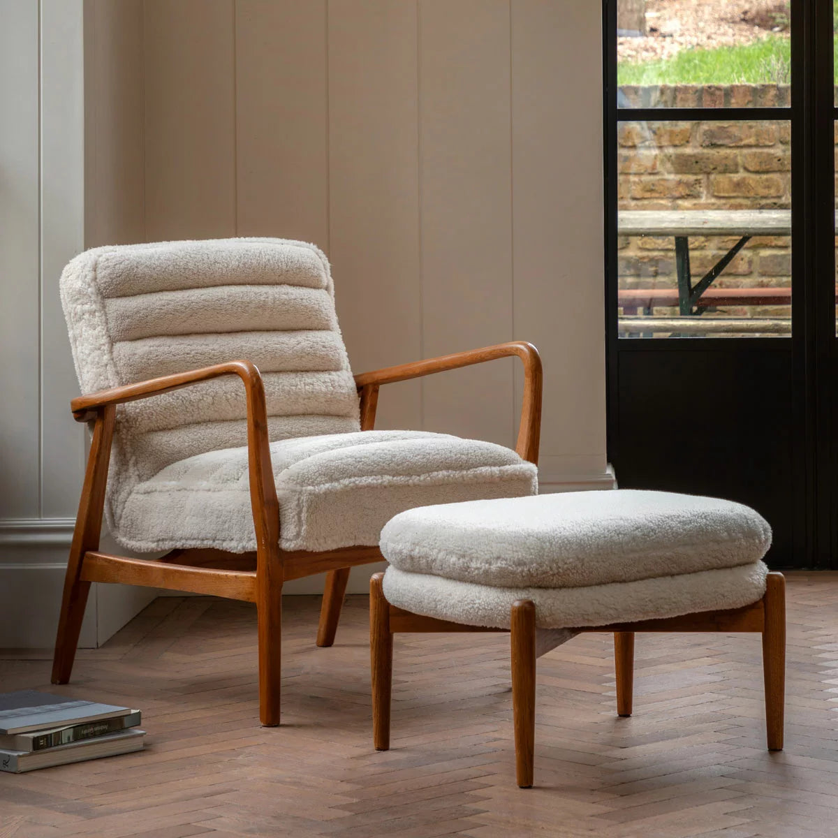 A three-quarter view of the Gallery Datsun Sheepskin Fabric Armchair showcasing its soft cream upholstery, curved wooden armrests, and natural ash wood frame in a bright living room corner.