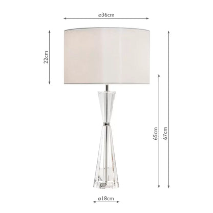 Luxurious Risha table lamp featuring a heavy, faceted hourglass-shaped crystal base, polished nickel hardware, and an elegant ivory faux silk drum shade styled in a contemporary living room interior.