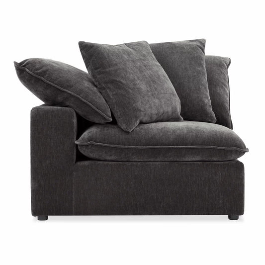A close-up shot of the Aiden & Ivy Sereen dark grey fabric corner chair in a bright, modern living room, highlighting its textured charcoal upholstery and two matching feather-filled cushions.