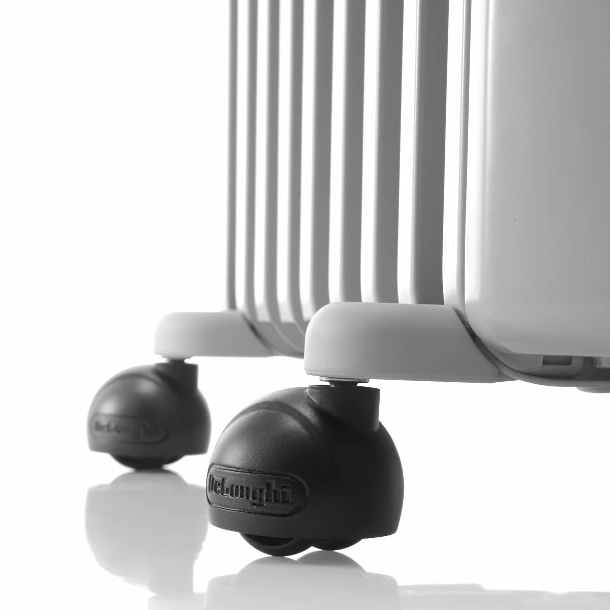 White De'Longhi Radia S 1.5kW oil filled radiator standing on a wooden floor in a modern living room setting showing pre-assembled castors and control knobs.