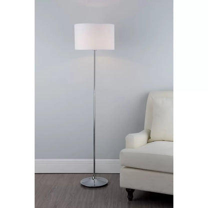 A side-angle shot of the Delta floor lamp featuring a polished chrome tear-shaped base and a clean ivory cotton drum shade casting a soft, warm glow in a contemporary living room corner.
