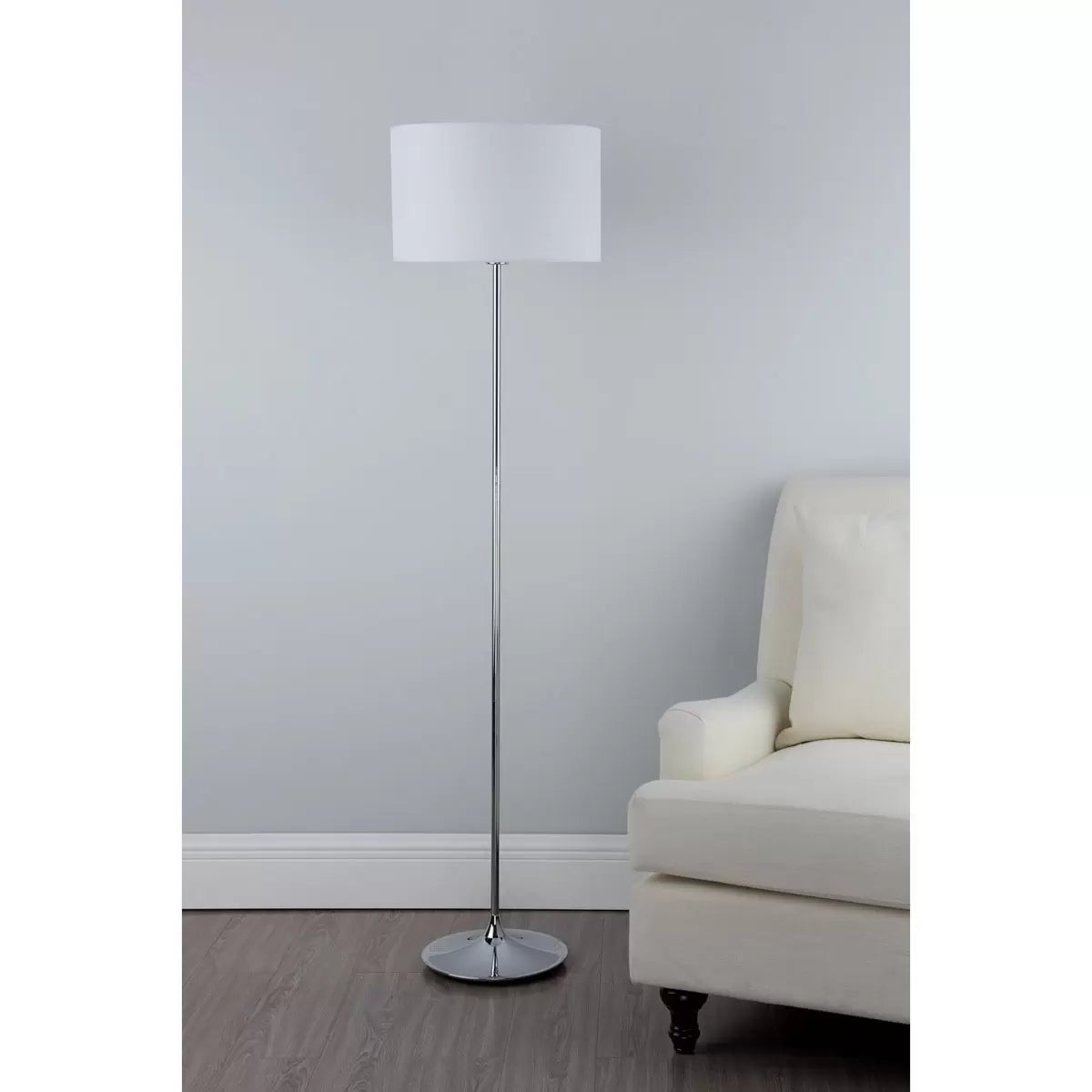 A side-angle shot of the Delta floor lamp featuring a polished chrome tear-shaped base and a clean ivory cotton drum shade casting a soft, warm glow in a contemporary living room corner.