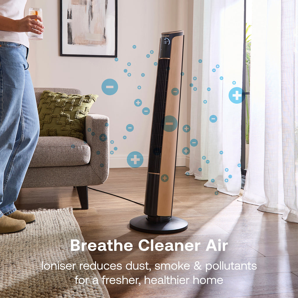 A tall, slender black and copper Dimplex Ion Fresh tower fan standing elegantly on a hardwood floor next to a modern armchair.