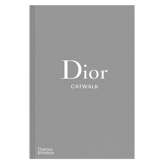 Front angle of the Dior Catwalk hardcover book with gray cloth binding and clean embossed lettering placed on a sleek table.