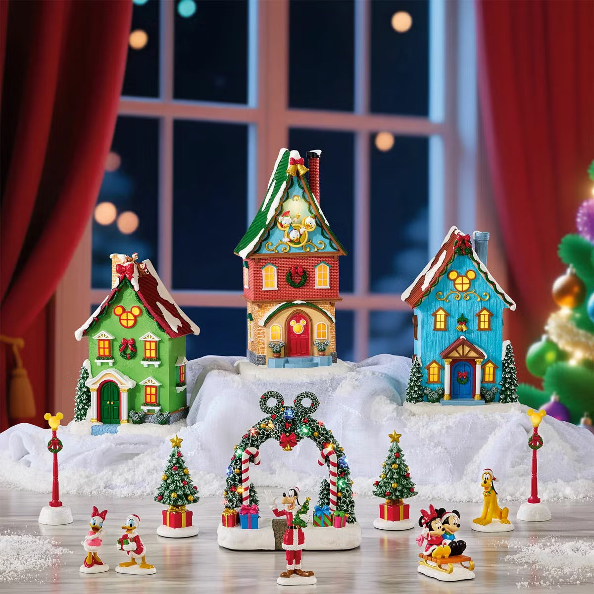 Complete 13-piece lighted Disney Christmas village featuring hand-painted Mickey Mouse figures, glowing LED snow-covered houses, and illuminated archway on a wooden table.