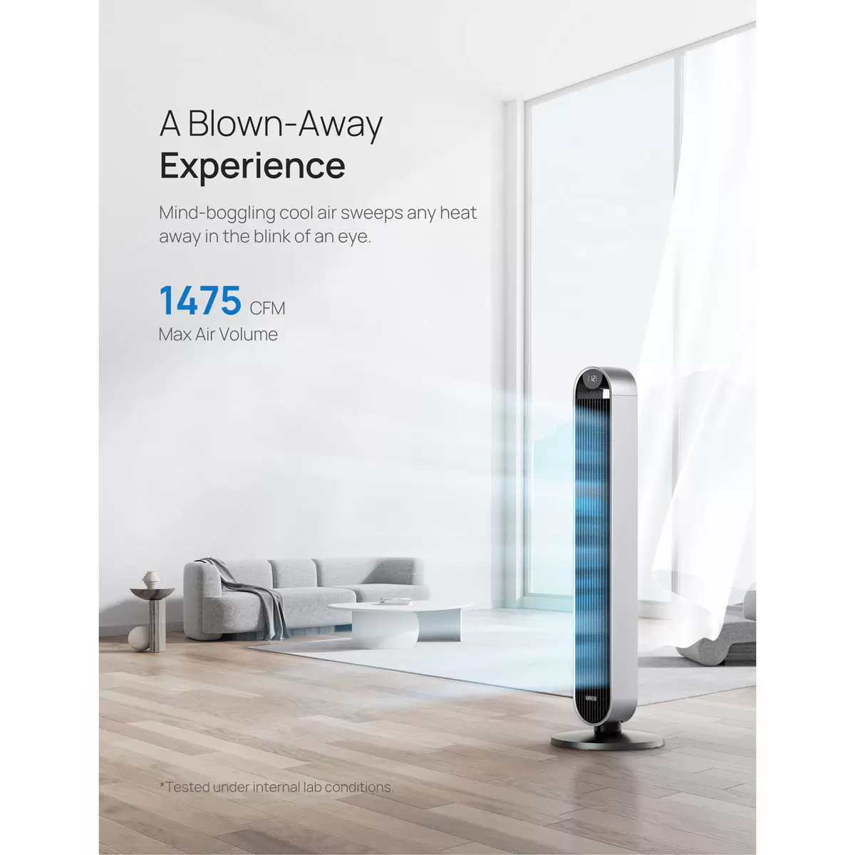 Silver Dreo Pilot Max DR-HTF004S smart tower fan standing upright on a dark hardwood floor against a minimalist white living room wall.