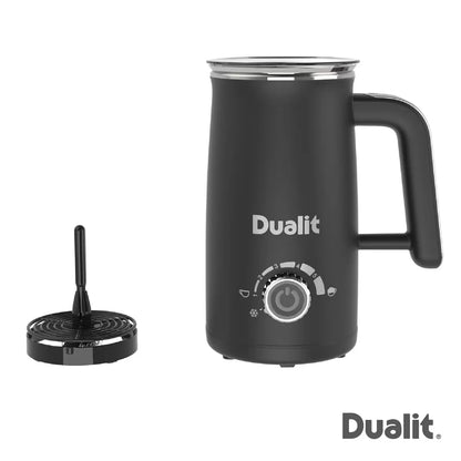 Dualit Milk Frother Max in black and stainless steel sitting on a wooden kitchen counter next to a mug of hot chocolate with chocolate sachets alongside.