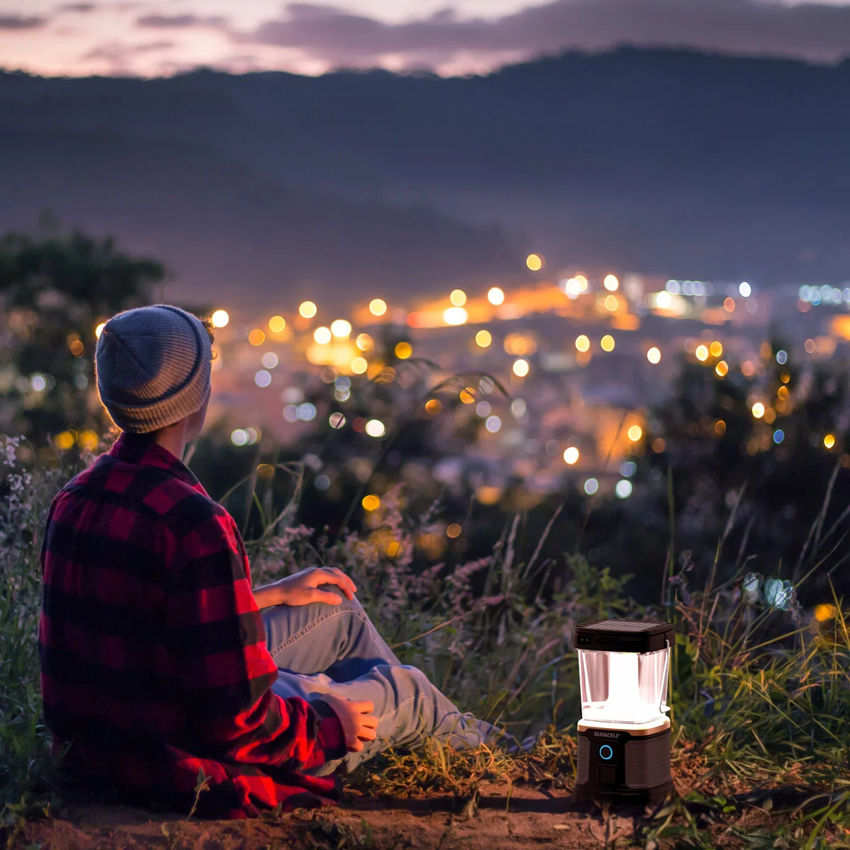 Rugged black Duracell 3000 lumen outdoor lantern sitting on a dark wooden picnic table with its top solar panel and wireless charging port illuminated.