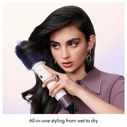 Dyson Airsmooth styling brush in Ceramic Pink with teardrop brush head and soft dual bristles sitting on a vanity table.