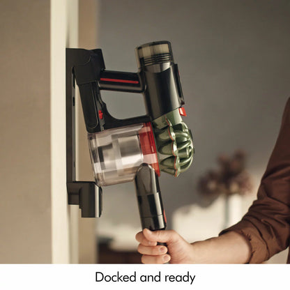 Side angle view of the nickel and purple Dyson V8 Cyclone stick vacuum mounted in its wall dock on a plain wall setup.