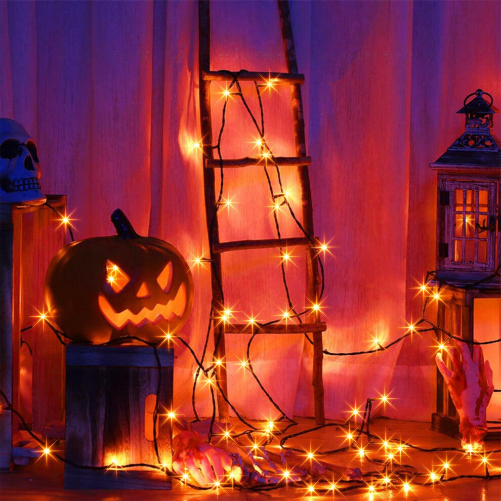 A 20m string of 200 orange LED fairy lights on a black cable glowing across an outdoor haunted house display at night.