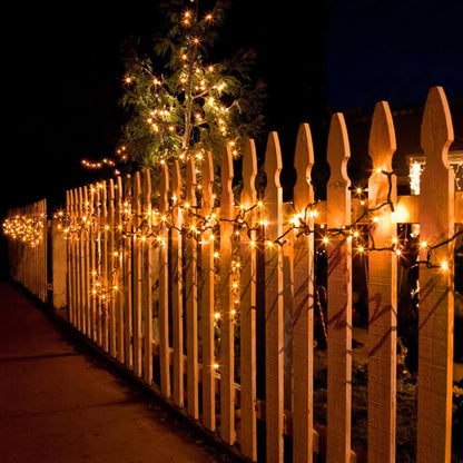 A 20m string of 200 orange LED fairy lights on a black cable glowing across an outdoor haunted house display at night.